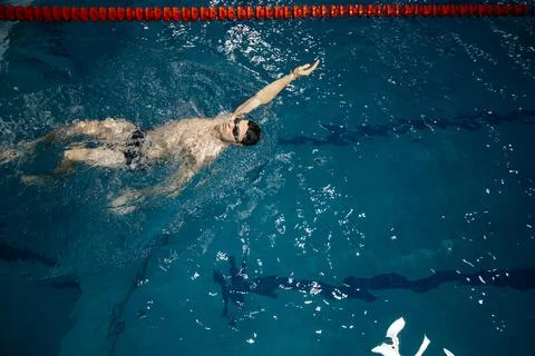 Man in the pool. Floating on his back. A swimmer trains in the pool on the track Stock Photos