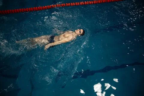 Man in the pool. Floating on his back. A swimmer trains in the pool on the track Stock Photos