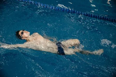 Man in the pool. Floating on his back. A swimmer trains in the pool on the track Stock Photos