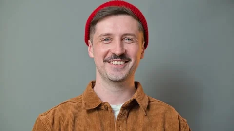A man poses in multiple angles wearing a red beanie and brown jacket. His 動画素材 337642573