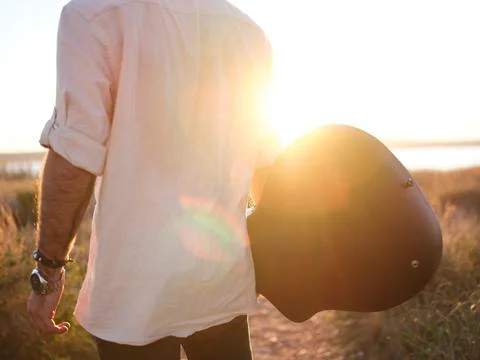 Man posing backwards holding his guitar and watching the sunset Stock Photos