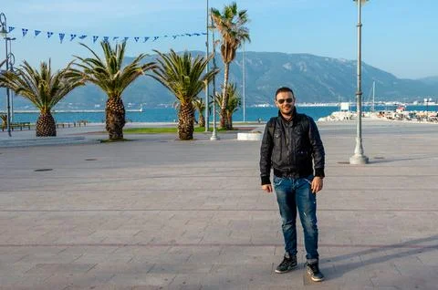 Man Posing on Corinth Seafront Promenade with Flags and Palms. Foto stock