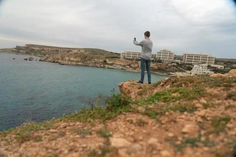 Man posing in front of Golden beach, Malta under the clouds with turquoise wa Stock Photos