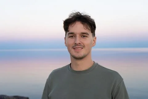 Man posing in front of a serene landscape at dusk, looking at camera. Stock Photos