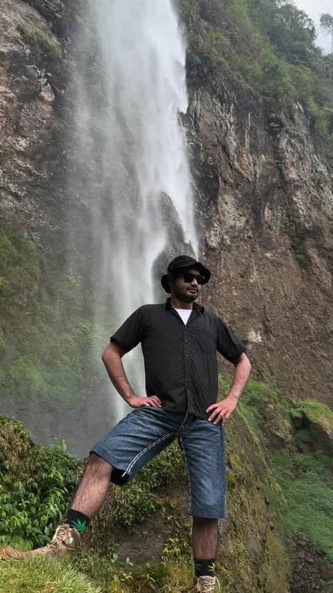 Man Posing in Front of Waterfall, Lush Green Nature, Vertical Full Shot Stock Footage 323912506
