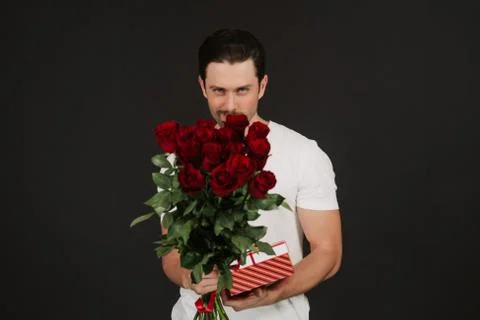 Man is posing on grey background with gift box and red roses in hands Stock Photos