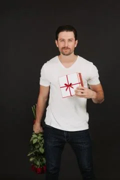 Man is posing on grey background with gift box and red roses in hands Stock Photos