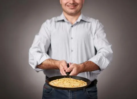 Man posing with a pancake in a pan, white shirt and pants, gray background, s Stock Photos
