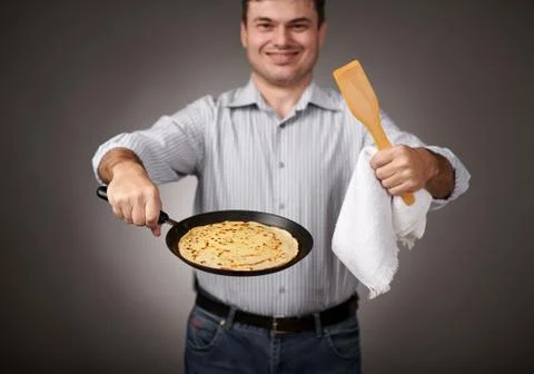 Man posing with a pancake in a pan, white shirt and pants, gray background, s Stock Photos