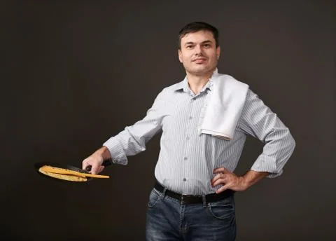 Man posing with a pancake in a pan, white shirt and pants, gray background Stock Photos