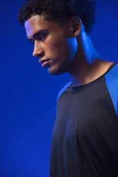Man posing tilting head down wearing blue-shoulder shirt on studio backdrop lit Stock Photos