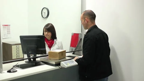 Man posting out a package / Parcel at the Post Office Counter - Female assistant Stock Footage 131841327
