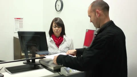 Man posting out a package / Parcel at the Post Office Counter - Female assistant Stock Footage 131841345