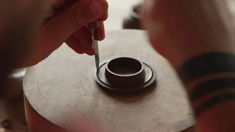 Man potter cuts off excess clay on a lid for a clay teapot on a potter's wheel Stock Footage 145534558