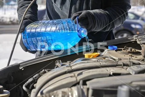 Man pouring an antifreeze liquid in a windshield washer tank of a car Stock-Fotos
