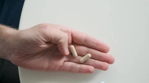 Man pouring beige probiotic capsules in hand from medicine bottle. Nutritional Stock Footage 315860088