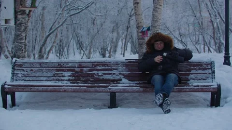 Man pouring coffee into a thermos while sitting on a park bench Stock Footage 179998242