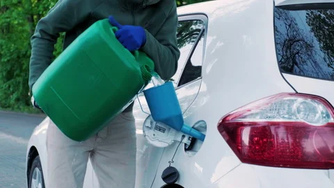 A man pouring gasoline into an empty fuel tank from a plastic red gas can. Stock Footage 195695628