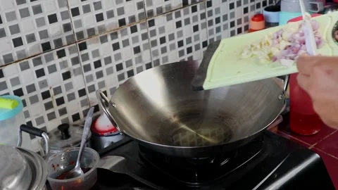 A man is pouring shallots and garlic into a wok to cook into fried rice. Stock Footage 242569599