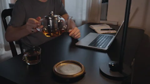 Man pouring tea at home workspace with laptop Stock Footage 315959535