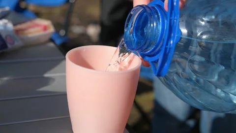 Man pouring water from bottle to plastic cup on nature in sunny day. Stock Footage 277869067
