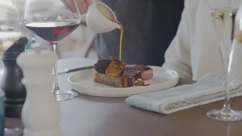 A man is pouring wine into a glass while a woman sits at a table with a plate of Stock Footage 306576514