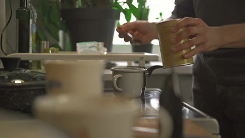 A man pours cocoa into a mug from a jar with a spoon early in the morning Stock Footage 172575520