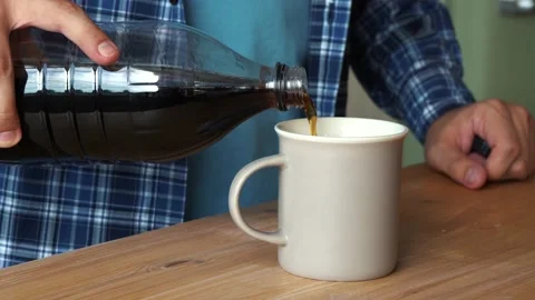 Man pours cola into a mug while sitting in the kitchen Stockbeeldmateriaal 157367407