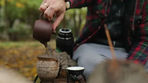 A man pours dark pu-erh from a clay teapot into a special clay pot. outdoor Stock Footage 220415321