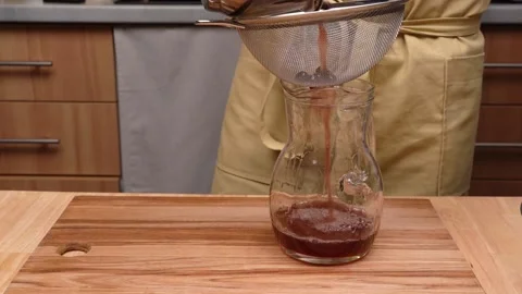 A man pours a drink with pulp through a sieve into a glass carafe Vidéo 236888601