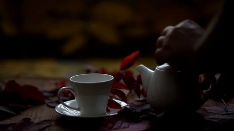 A man pours hot tea into a cup. On the table is a decoration of autumn leaves. Stock Footage 120426844