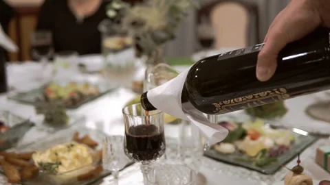 A man pours red wine into a glass from a bottle during a family dinner. The wait Stock Footage 245352001