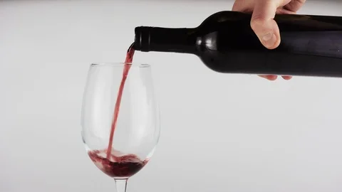 A man pours a red wine into a transparent glass. A glass stands on a white Видео 88823323