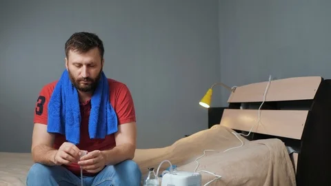 Man pours saline solution for inhalation into nebulizer. Young man sits alone in 스톡 동영상 123276788