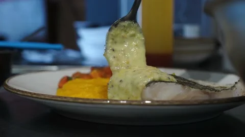 Man pours sauce from a spoon into a dish before serving it in restaurant kitchen Stock Footage 141245571