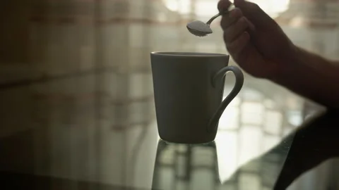 Man pours sugar into a mug with a spoon and stirs, on a light window background Stock Footage 134477439