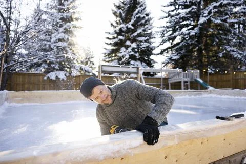 Man with power drill constructing ice rink in snowy backyard Stock Photos