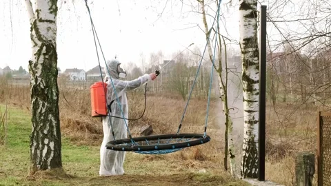 Man in PPE and mask spraying with a knapsack sprayer birch trees with fungicide Stock Footage 308397642