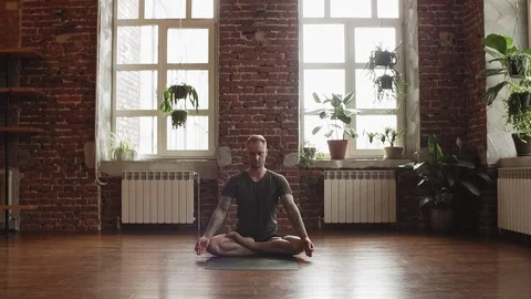 Man practice lotus pose in yoga studio with brick wall. Man making yoga pose Video stock 105166161