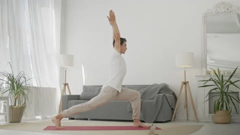 Man Practice Warrior Yoga Pose in Living Room. Sporty Man Doing Yoga for Body Stock Footage 134737187