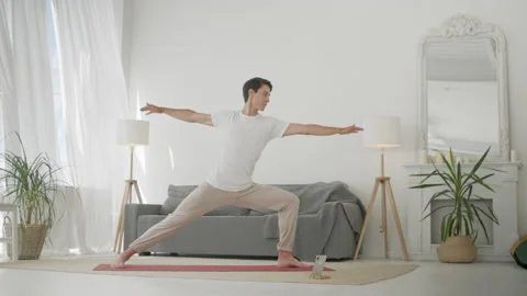 Man Practice Warrior Yoga Pose in Living Room. Sporty Man Doing Yoga for Body Stock Footage 134738190