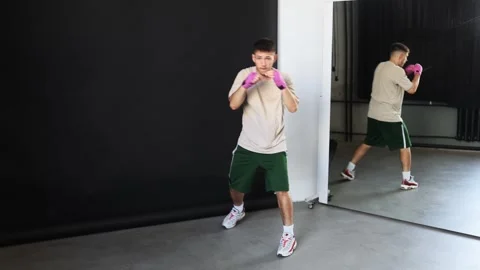 Man practices boxing techniques in a gym with a mirror reflection Stock Footage 312383779