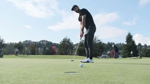 Man practices putting on golf course and narrowly misses the hole Stock Footage 312697915