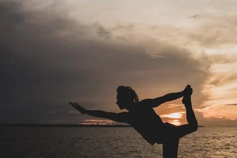 A man practices a yoga posture at sunset. In the background the waters of Bla Stock Photos