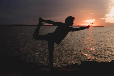A man practices a yoga posture at sunset. In the background the waters of Bla Stock Photos