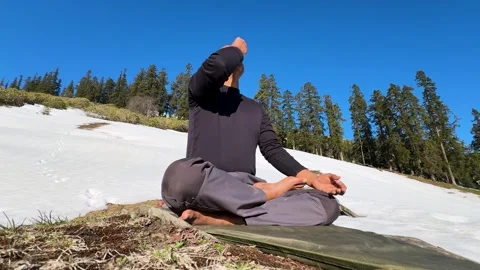Man practicing anulom vilom pranayam sitting on mat in snow covered hills 動画素材 333700914