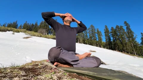 Man practicing bhramari pranayama sitting on mat in snow covered hills 库存影片 334330886