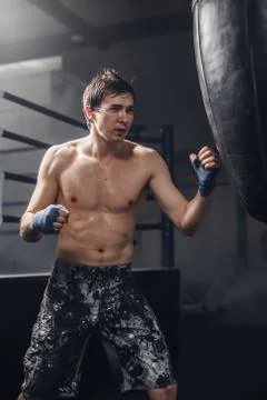Man practicing boxing on big black bag in gym Stock Photos