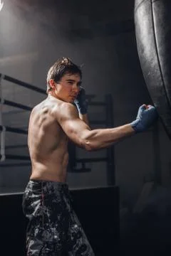 Man practicing boxing on big black bag in gym Stock Photos
