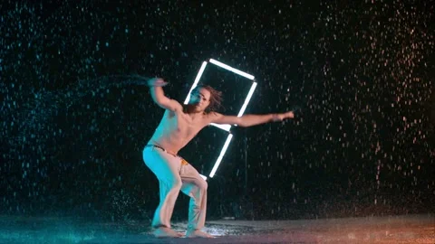 Man practicing Capoeira heel spin kicks, dancing in wet rain studio Stock Footage 130776719